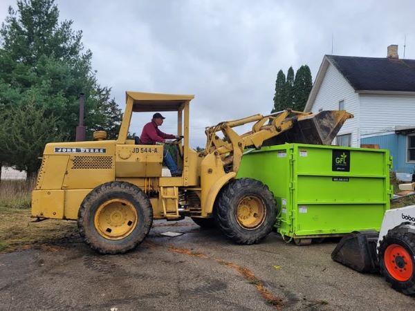 stan-loading-dumpster-yellow-skidloader