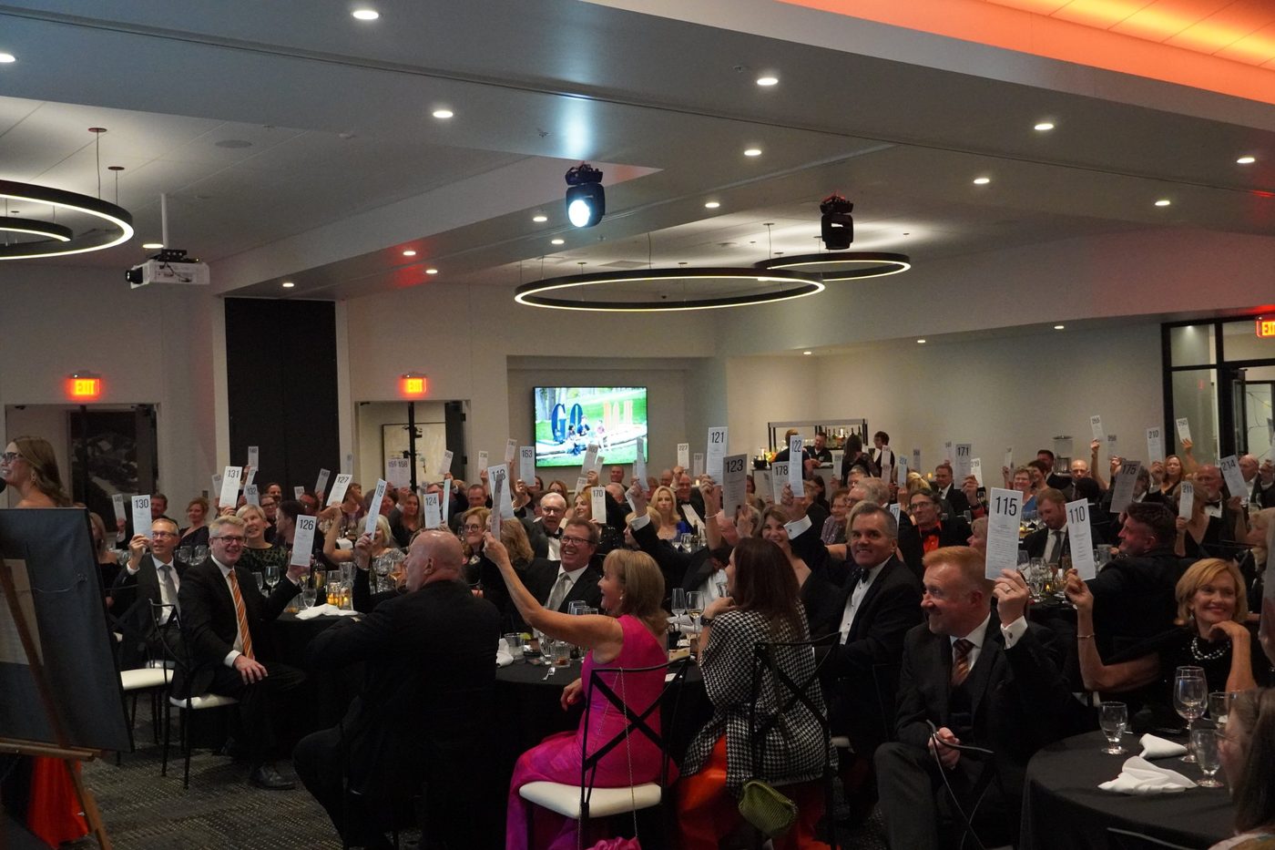 A full room of gala guests raising numbered bid cards during a paddle raise